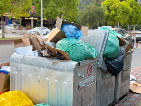 Overflowing garbage container with plastic bags and cardboard. Urban waste, pollution and...
