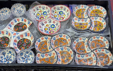 Handmade ceramic bowls with traditional colorful patterns stacked in market stall. Craftsmanship,...