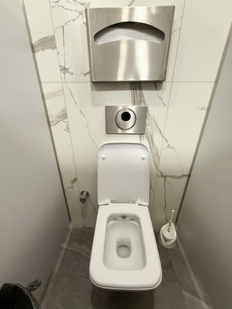 Toilet in public restroom with sanitary equipment and marble wall. Hygiene, cleanliness, and facility maintenance in modern service spaces.の写真素材