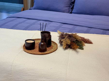 Bed with blue bedding and decorative set of candle, diffuser, and dried flowers. Comfort, lifestyle, and cozy atmosphere in modern interior design.の写真素材