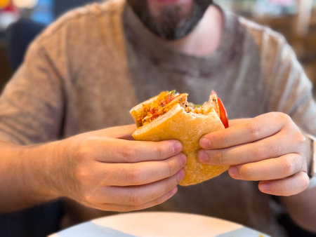 Close-up of hands holding bitten sandwich with visible filling. Food, consumption and lifestyle moments in daily eating habits.の写真素材