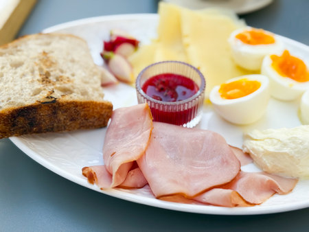 A breakfast plate with ham, cheese, eggs, bread, and jam served with tea. Nutrition, lifestyle, and dining culture illustrate morning meal, tradition, and balanced food choices.の写真素材