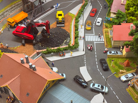 A miniature diorama shows cars, houses, and an excavator working on a road scene. Urban model, construction, and transportation highlight detail, creativity, and social interaction.の写真素材