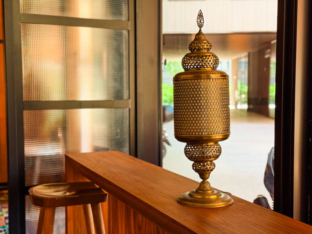 Golden table lamp with intricate perforated design placed in cozy interior. Craftsmanship, tradition, and cultural heritage expressed through ornamental furnishing and warm light.の写真素材