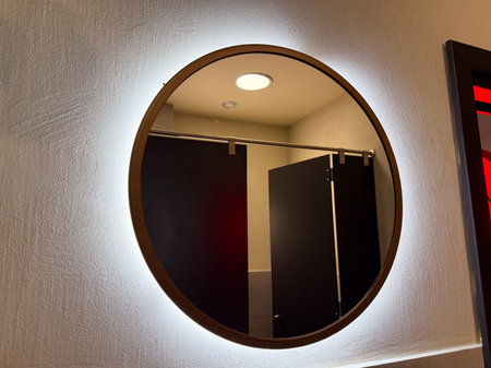 Round illuminated mirror glowing on bathroom wall reflecting interior space. Hygiene, design, and furnishing symbolizing cleanliness, atmosphere, and daily lifestyle detail.の写真素材