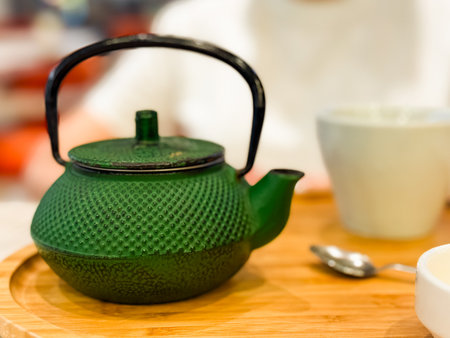 Green cast iron teapot with cup and spoon on wooden tray. Beverage, hospitality, and lifestyle highlighting tradition, refreshment, and cultural dining ritual.の写真素材