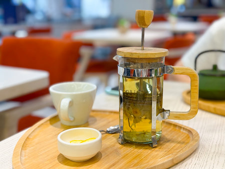 Glass french press with herbal tea and cup on wooden tray. Beverage, wellness, and hospitality highlighting relaxation, natural nutrition, and daily refreshment.の写真素材