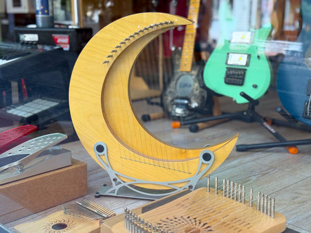Wooden crescent-shaped string instrument displayed in a shop window with guitars. Creative design,...
