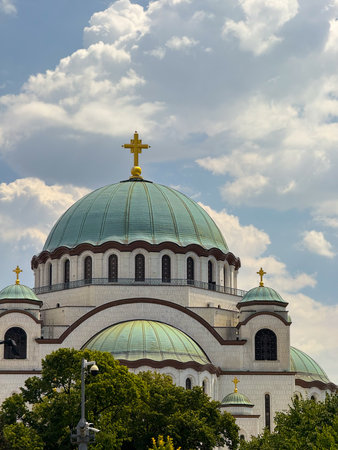 Saint Sava temple dome with golden crosses under clouds in Belgrade Serbia surrounded by trees. Religious architecture, Christian orthodoxy, cultural landmark, faith, tradition, history and spiritual heritage.の写真素材
