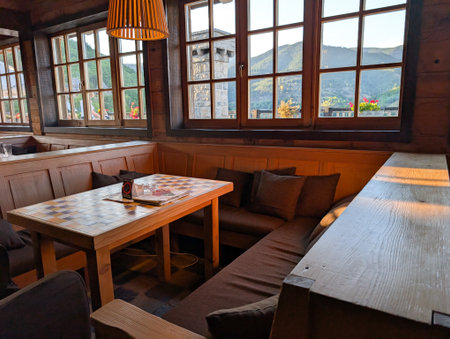 Cozy wooden interior with mountain view through wide windows. Warm light, rustic furniture, and...