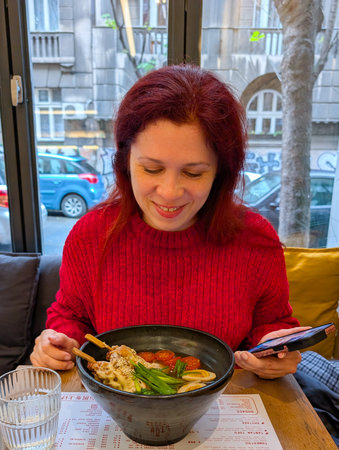 Woman smiling with ramen bowl on restaurant table. Joyful dining, food culture, and lifestyle...
