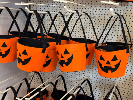 Orange felt buckets with jack o lantern faces and black handles on retail display. Halloween container, candy collection, seasonal festivity, tradition, playful celebration and autumn folklore.の写真素材