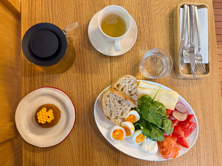 Morning meal with tea, honey dessert, eggs, vegetables, cheese, and bread arranged on wooden surface top view. Balanced breakfast symbolizing comfort and slow living.の写真素材