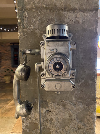 Retro rotary telephone mounted on raw concrete surface in dimly lit interior. Industrial heritage,...