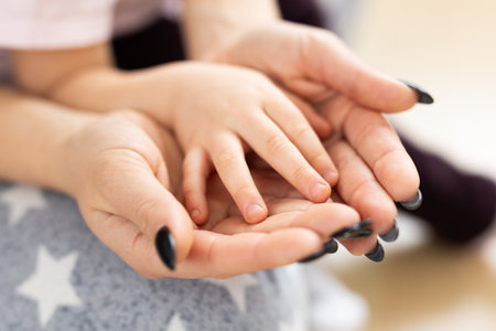 Close-up of mother holding her child small hands gently in a warm light. Family intimacy, protection, tenderness, and emotional closeness in everyday parentingの写真素材