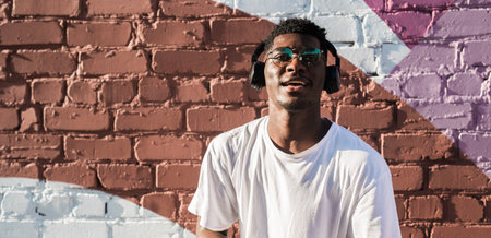 Young african american man dancing with headphones on colorful wall background. Concept of music,...