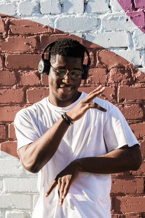 Young african american man dancing with headphones on colorful wall background. Concept of music,...