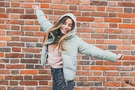 Joyful woman in pastel jacket raising arms and smiling outdoors. Urban freedom, positive energy, and expression of happiness in city life.の写真素材