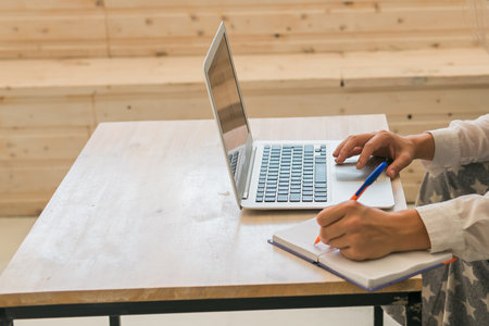 Female freelancer writing notes in notebook while working on laptop at home. Focus, discipline, and balance between work and creativity.の写真素材