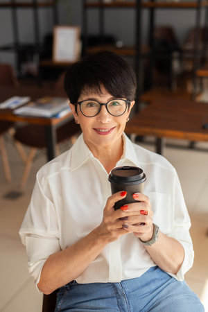 Smiling woman holding coffee cup while sitting in modern interior. Positivity, confidence, and balance in everyday lifestyle and self-care.の写真素材