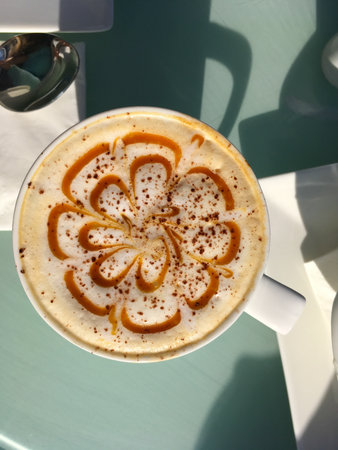 Cup of cappuccino with caramel pattern on foam. Coffee culture, morning routine, and cozy cafe...