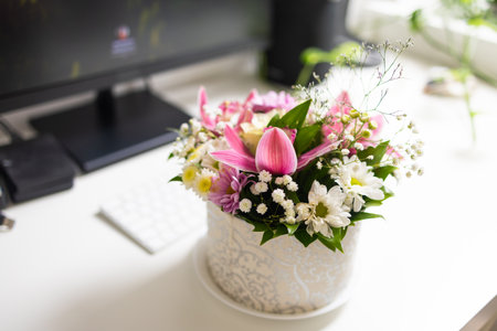 Floral bouquet near computer monitor and keyboard. Harmony of work, nature, and aesthetic minimalism in home office.の写真素材