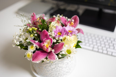 Elegant bouquet of pink orchids and daisies on white desk. Balance of work, beauty, and peaceful home ambiance.の写真素材