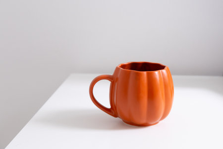 Orange mug on white surface. Simplicity, color focus, and warmth of minimal modern lifestyle. Copy spaceの写真素材
