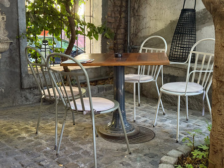Wooden table and metal chairs under tree shade in outdoor cafe. Peaceful corner, harmony of nature...