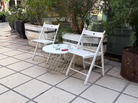 Two white chairs and round table on tiled street terrace. Simplicity, quiet relaxation, and everyday...