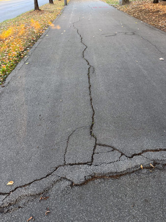 Cracked asphalt surface with visible damage lines. Urban decay, infrastructure wear, and passage of time.の写真素材