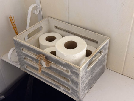 Wooden crate with toilet paper rolls on white shelf. Simple bathroom storage, everyday organization, and minimal hygiene detail.の写真素材