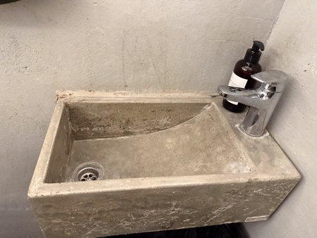 Minimal concrete sink with chrome faucet in small restroom. Industrial interior design, urban architecture, and functionality in everyday space.の写真素材