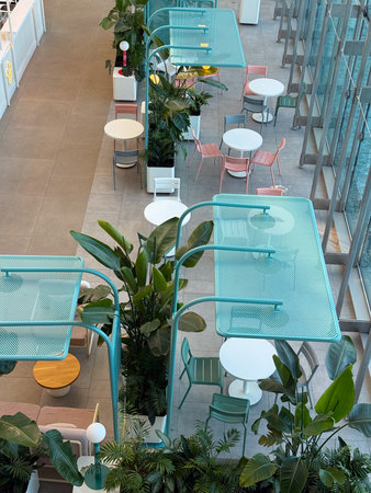 Cafe seating area with plants and pastel chairs under blue mesh shades. Social interaction, leisure,...