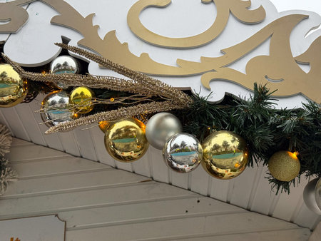 Golden and silver Christmas ornaments arranged under decorative sign on festive wooden stall roof. Holiday market decor, winter celebration atmosphere and traditional seasonal design.の写真素材