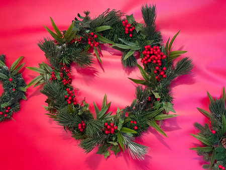 Green Christmas wreath with red berries on pink background. Modern festive decor, winter celebration and colorful holiday styling.の写真素材