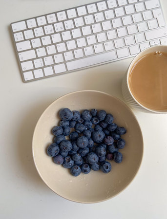 Blueberries in bowl with tea beside computer keyboard. Healthy snack routine, workday balance, calm...