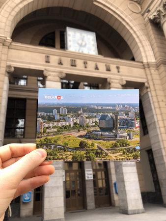 Minsk, Belarus - February 27, 2019: Hand holding postcard with Minsk city skyline in front of the...