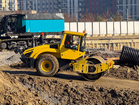 Yellow soil roller at construction site with high-rise buildings in background. Urban development,...