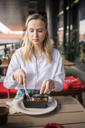 Woman eating moussaka at a cafe terrace during a relaxed afternoon break. Casual dining, urban food...