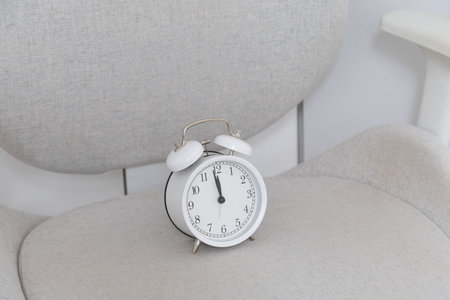 White alarm clock on chair. Minimalism, clarity, and peaceful rhythm of slow living lifestyle. Copy...