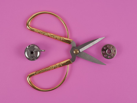 Accessories for sewing thread scissors needle and centimetre on a pink background