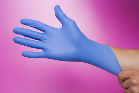 Hands wearing a blue latex glove, isolated on pinkの写真素材