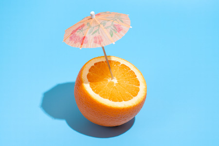 Fresh juicy orange with a cocktail umbrella isolated on blue background. Concept of Healthy eating and dieting. Drink conceptの写真素材