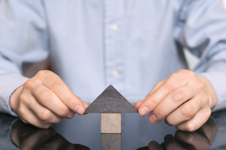Wooden toy house protected by hands. The concept of buying and selling real estate, rental housing,...