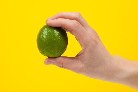 Ripe juicy lime in hand isolated on yellow background. Healthy eating and dieting conceptの写真素材