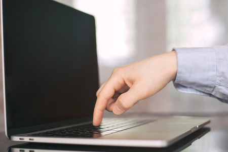 One single finger pressing keyboard button in laptop with blurry background. Ordering or choosing...