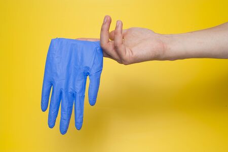 Blue rubber glove on a man hand isolated on yellowの写真素材