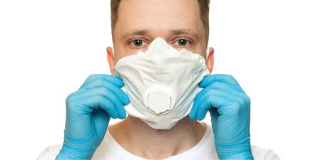 Young surgeon doctor in latex protective gloves puts on white protection mask on whiteの写真素材