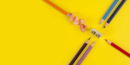Some colored pencils of different colors and a pencil sharpener and pencil shavings on the yellowの写真素材
